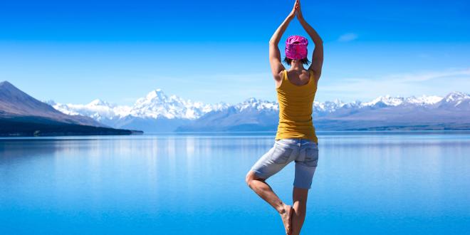 A young woman doing a yoga pose for balance on a rock overlooking a lake.