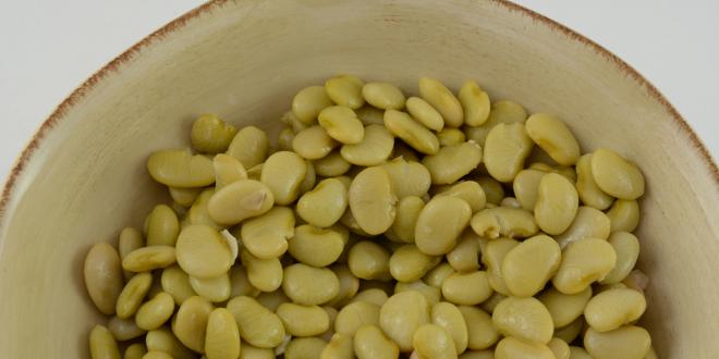 Top view of lima beans in cream colored rustic bowl with a white background.